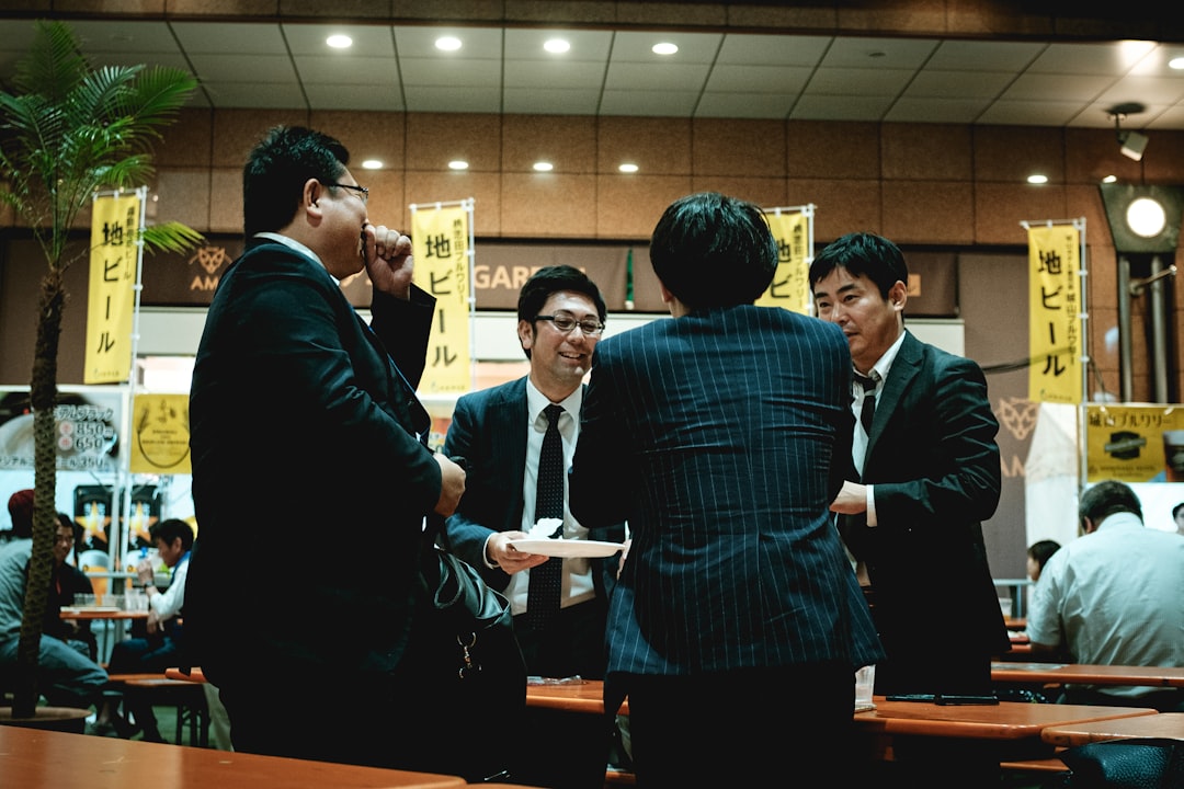 Two men in suits, one japanese one chinese, shaking hands but looking unhappy