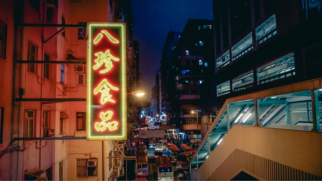 Crowded street scene in Hong Kong at night, with bright neon signs and a mix of modern and traditional architecture.