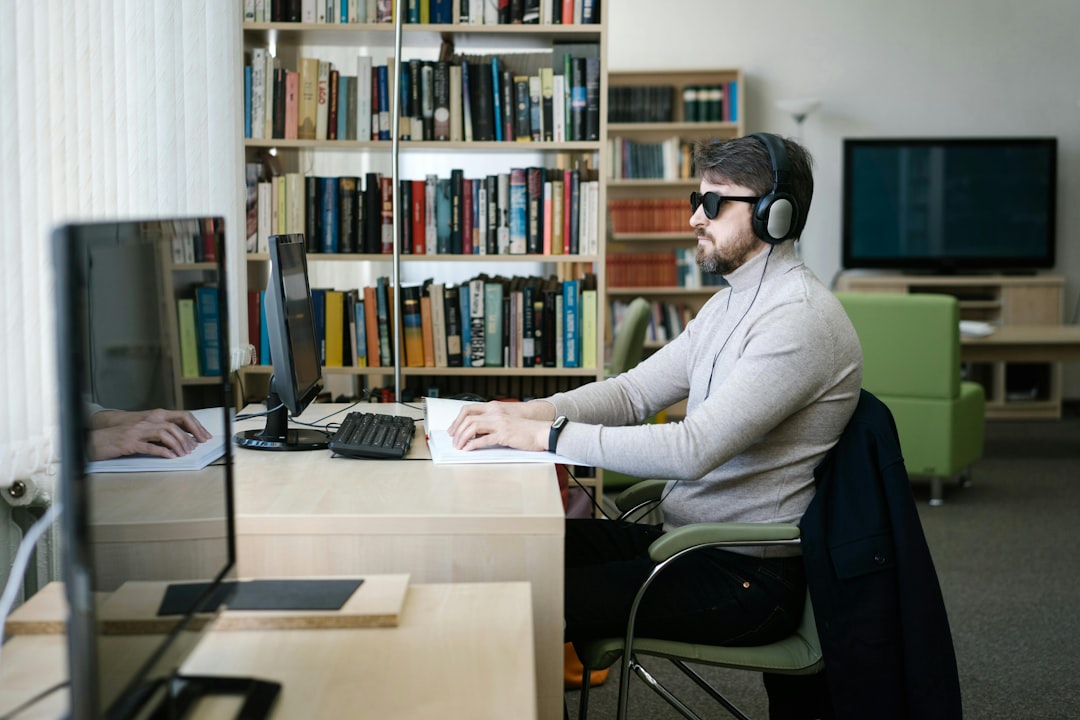 Man in suit sitting at desk in dim office, looking stressed and holding his head